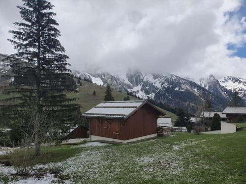 a barn in a field with mountains in the background at Appartement 25m2 à Manigod, col merdassier. in Manigod