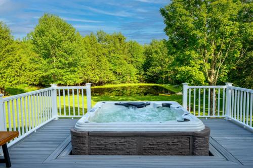 a hot tub on a deck next to a pond at Mountain Blue Vista - Luxury retreat near Ski resorts with Pond, Firepit and Hot Tub in Windham