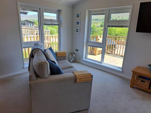 a living room with a couch and two windows at Diddly Squat Lodge with hot tub, Pendle View Holiday Park in Clitheroe