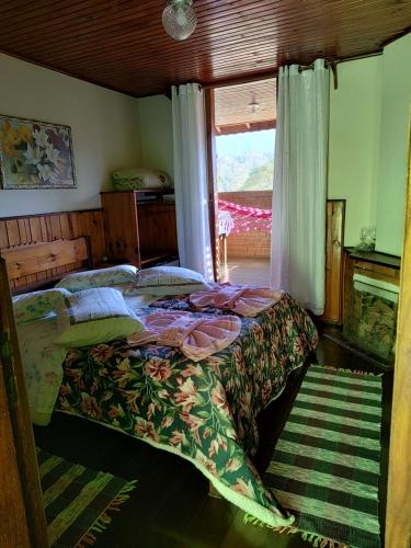 a bed in a room with a window and a bedspread at Pousada Solar das Flores Maringá RJ Visconde de Mauá in Visconde De Maua