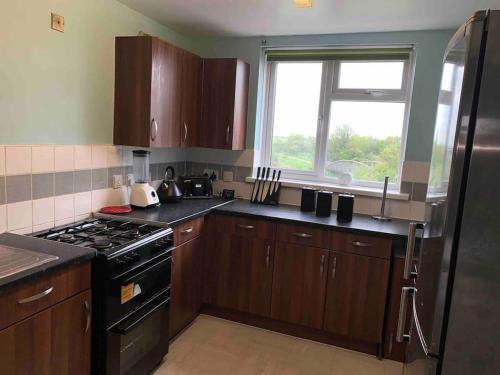 a kitchen with wooden cabinets and a stove and a window at Two bed flat stylishly furnished in Purfleet