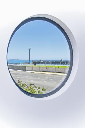 a round window in a white wall with a view of the ocean at Burnie by the Bay Apartments in Burnie