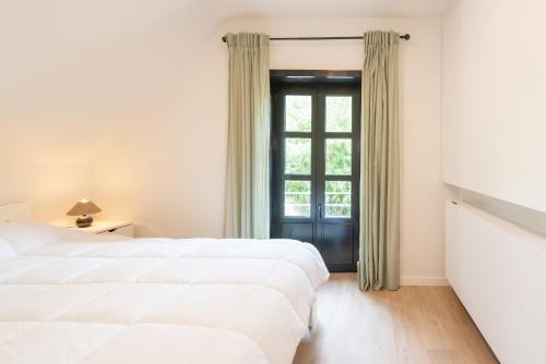 a white bedroom with a large bed and a window at De Burg in Alveringem
