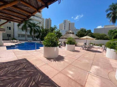 un patio con piscina, mesas y sombrillas en Fresca estancia en zona Dorada con Alberca/Playa!, en Acapulco