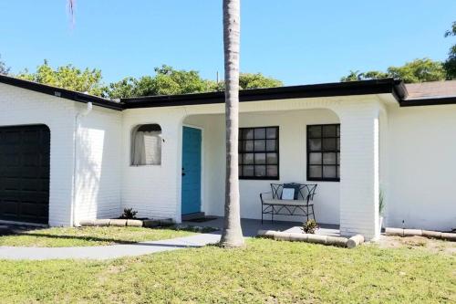 a white house with a blue door and a palm tree at Whole House+Renovated+Pool+Lanai+BBQ+Close to All in West Palm Beach