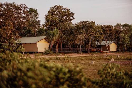 two buildings in a field with trees in the background at Bamurru Plains in Point Stuart