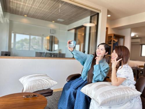Dos mujeres sentadas en un sofá tomando una foto de sí mismas en Garland Court Usami Private Hot Spring Condominium Hotel, en Ito