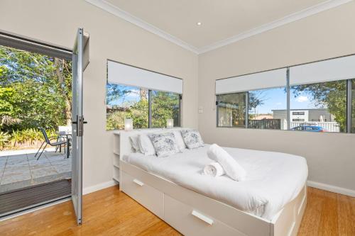 a white bedroom with a bed and windows at Kingston Gardens by Experience Jervis Bay in Huskisson