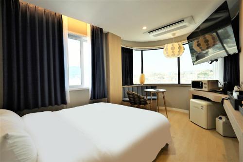 a hotel room with a white bed and windows at De Lamour Hotel in Tongyeong