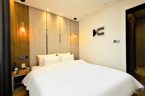 a bedroom with a large white bed and a desk at De Lamour Hotel in Tongyeong