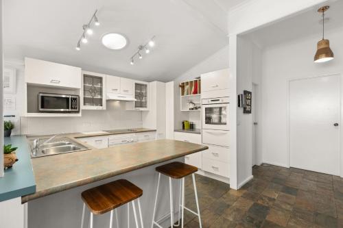 a kitchen with white cabinets and a counter with stools at Kingston Cottage by Experience Jervis Bay in Huskisson