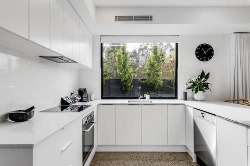 a white kitchen with white cabinets and a window at Vale 194 - Newly built in McLaren Vale - 5 holiday homes with king size beds in McLaren Vale