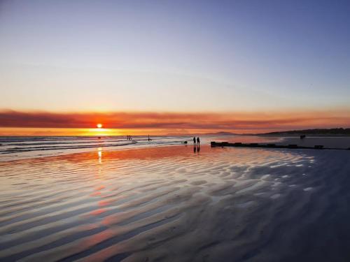 a person standing on a beach at sunset at OysterCatcher Self-Catering Accommodation Strand in Cape Town