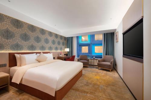 Guangzhou Wogo Yuanbao Hotel - Zhujiang New Town في قوانغتشو: غرفة فندقية بسرير وتلفزيون بشاشة مسطحة