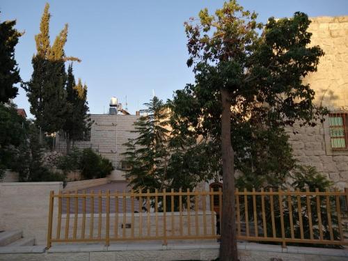 a wooden fence with a tree in front of a building at Lamar Guesthouse - Hebron in Hebron