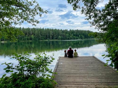 a man and two children sitting on a dock on a lake at Żurawi Staw- siedlisko obok Augustowa in Augustów