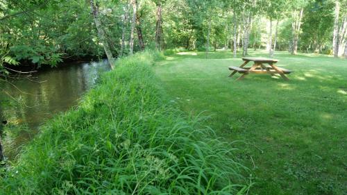 a picnic table sitting in the grass next to a river at Les Chalets du Moulin de Valade in Condat-sur-Trincou