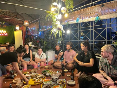 un grupo de personas sentadas alrededor de una mesa con comida en The Like Hostel & Cafe, en Ho Chi Minh