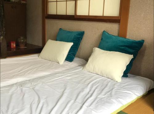ein weißes Bett mit zwei blauen Kissen darauf in der Unterkunft TOMO HOUSE in Taketoyo