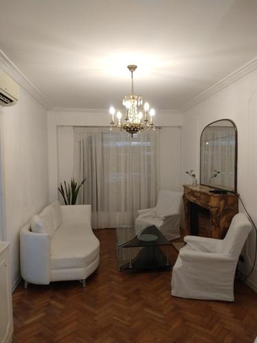 una sala de estar con muebles blancos y una lámpara de araña. en las cañitas libertador en Buenos Aires