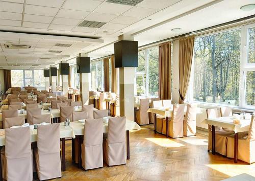 a restaurant with white tables and chairs and windows at SP ZOZ Sanatorium Uzdrowiskowe MSWiA Agat in Jelenia Góra
