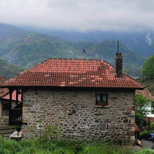 a stone building with a red tile roof with mountains in the background at La Casa Rectoral de El Tozu in Caso
