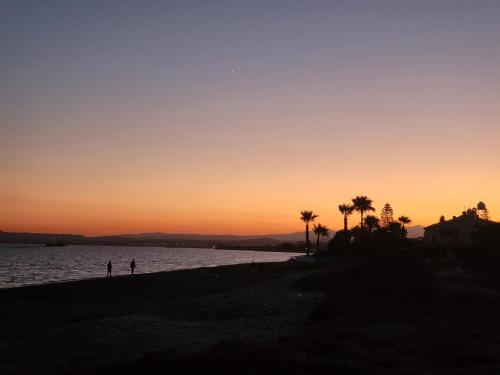 a sunset on a beach with palm trees and water at Mattis Seafront Beachhouse in Pervolia
