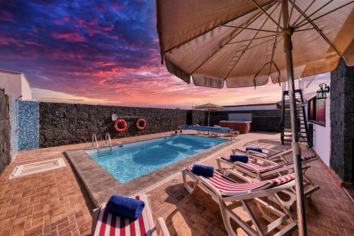 a swimming pool with chairs and an umbrella at Villa Aurelia - Pool, Jacuzzi, BBQ and Ping-Pong By Lanzarote Vacation Homes in Playa Blanca