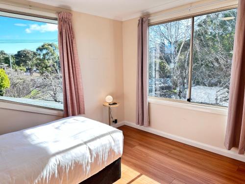 a bedroom with a bed and two large windows at Beach House Bellerive Hobart Eastern Shore in Bellerive