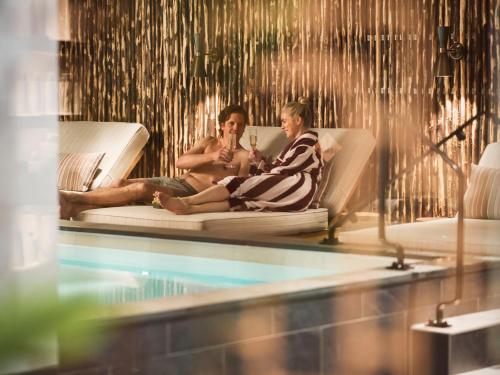 two women sitting on a couch next to a swimming pool at Elite Hotel Brage - Hotel & Spa in Borlänge