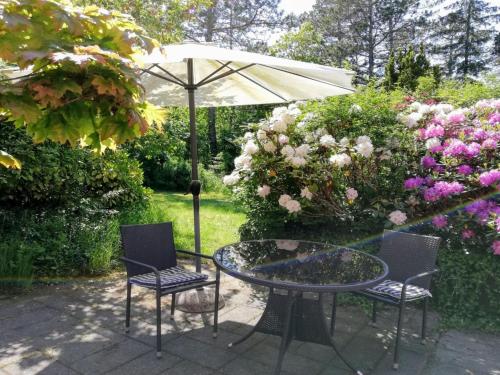 a table and chairs with an umbrella and flowers at Apartment Kolja - 3km from the sea in Western Jutland by Interhome in Blåvand