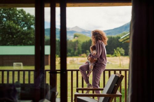a woman standing on a porch holding a child at Eco Village & Chalets Green Heaven in Mojkovac