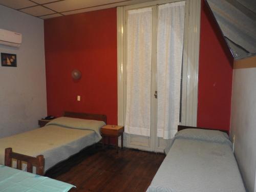 two beds in a room with red walls and a window at Hotel Ideal in Montevideo