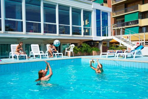 Dos personas están nadando en una piscina. en Ale Suite Sea Side View - Hotel Arizona, en Riccione