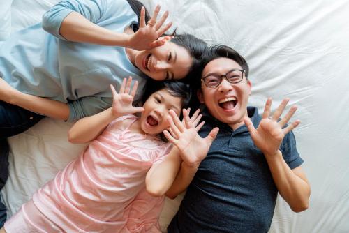 three people laying on a bed with their hands in the air at Golden Tulip Mandison Suites in Bangkok