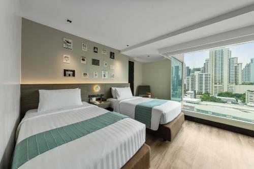 two beds in a hotel room with a large window at Golden Tulip Mandison Suites in Bangkok