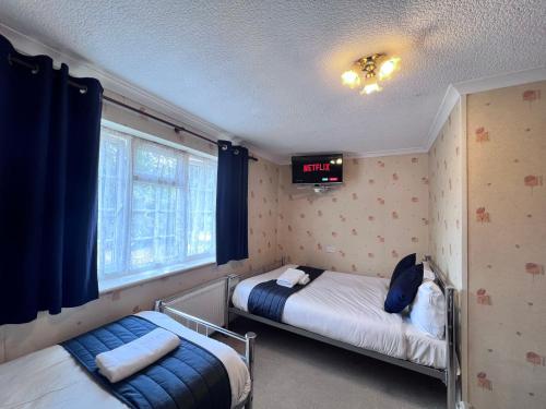a bedroom with two beds and a tv on the wall at All Seasons Gatwick Guest House & Parking in Horley