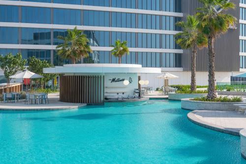 uma piscina em frente a um edifício com palmeiras em The WB Abu Dhabi, Curio Collection By Hilton em Abu Dhabi
