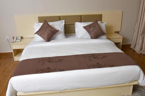 Cama grande con sábanas y almohadas marrones y blancas en Hotel Next en Masaka