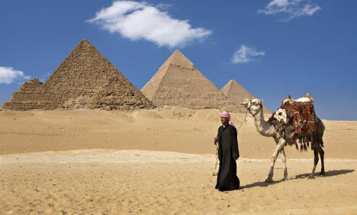 a man standing next to a camel in front of pyramids at Hilton Cairo Zamalek Residences in Cairo