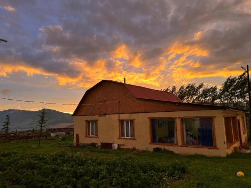 Ein Haus auf einem Feld mit Sonnenuntergang im Hintergrund in der Unterkunft Bulak in Tar-Suu
