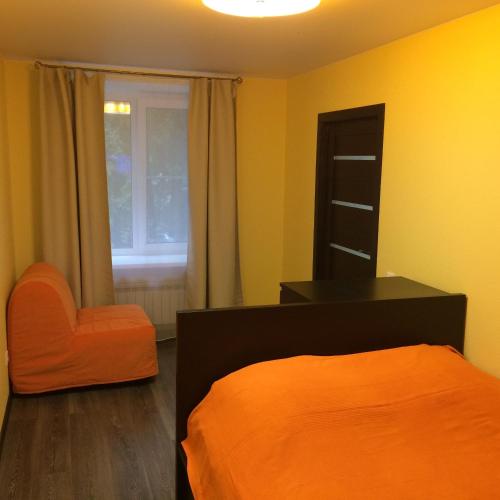 ヴェリーキー・ノヴゴロドにあるChudintseva 11のベッドルーム(オレンジ色のベッド1台、椅子付)
