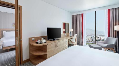 a hotel room with a bed and a desk with a television at Hilton Garden Inn Muscat Al Khuwair in Muscat