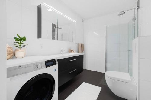 a white bathroom with a washing machine and a toilet at Bakklandets Perle 3-roms in Trondheim