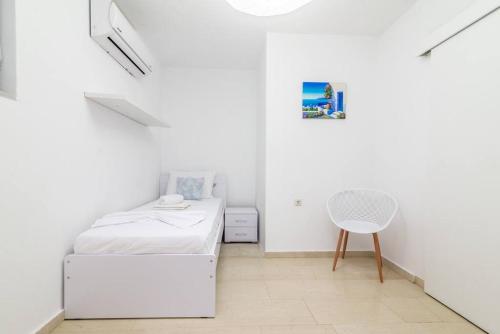 a white bedroom with a bed and a chair at The Holiday Choice 1 in Agios Nikolaos