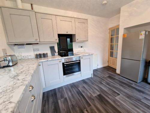una cucina con mobili bianchi e pavimento in legno di Chimes-Company & Family Stay, 2 Bedroom House + Free parking a Tamworth