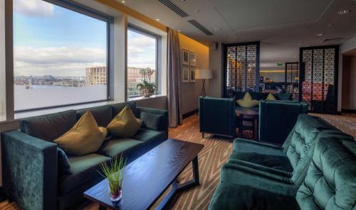 a living room with green couches and a large window at Hilton London Canary Wharf in London