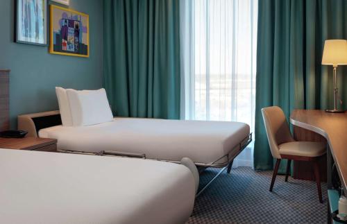 a hotel room with two beds and a desk and a window at Hampton By Hilton Edinburgh Airport in Ingliston