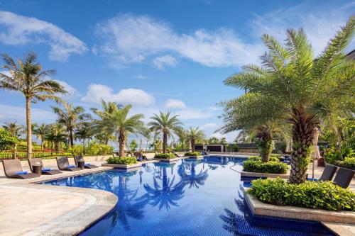 a swimming pool with palm trees and lounge chairs at Hilton Wenchang in Wenchang