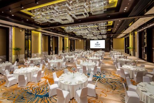 une salle de banquet avec des tables et des chaises blanches ainsi qu'un écran dans l'établissement Hilton Wenchang, à Wenchang